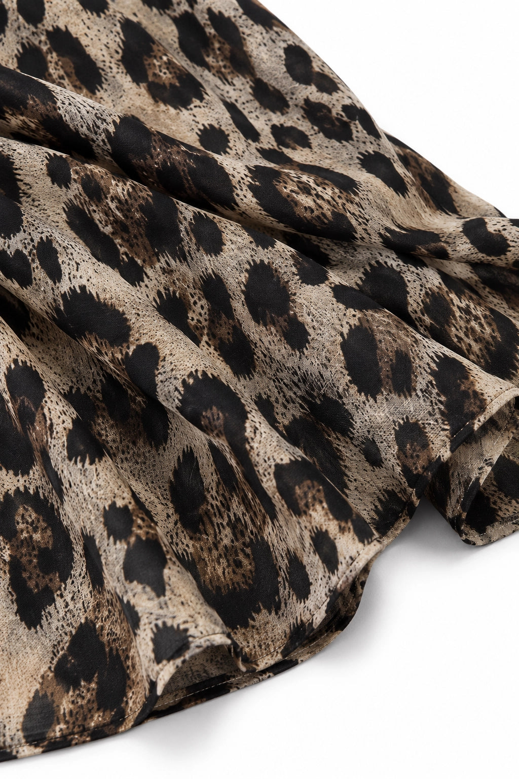 A close-up of draped leopard print fabric with a beige base and dark brown to black spots, shown against a plain white background.