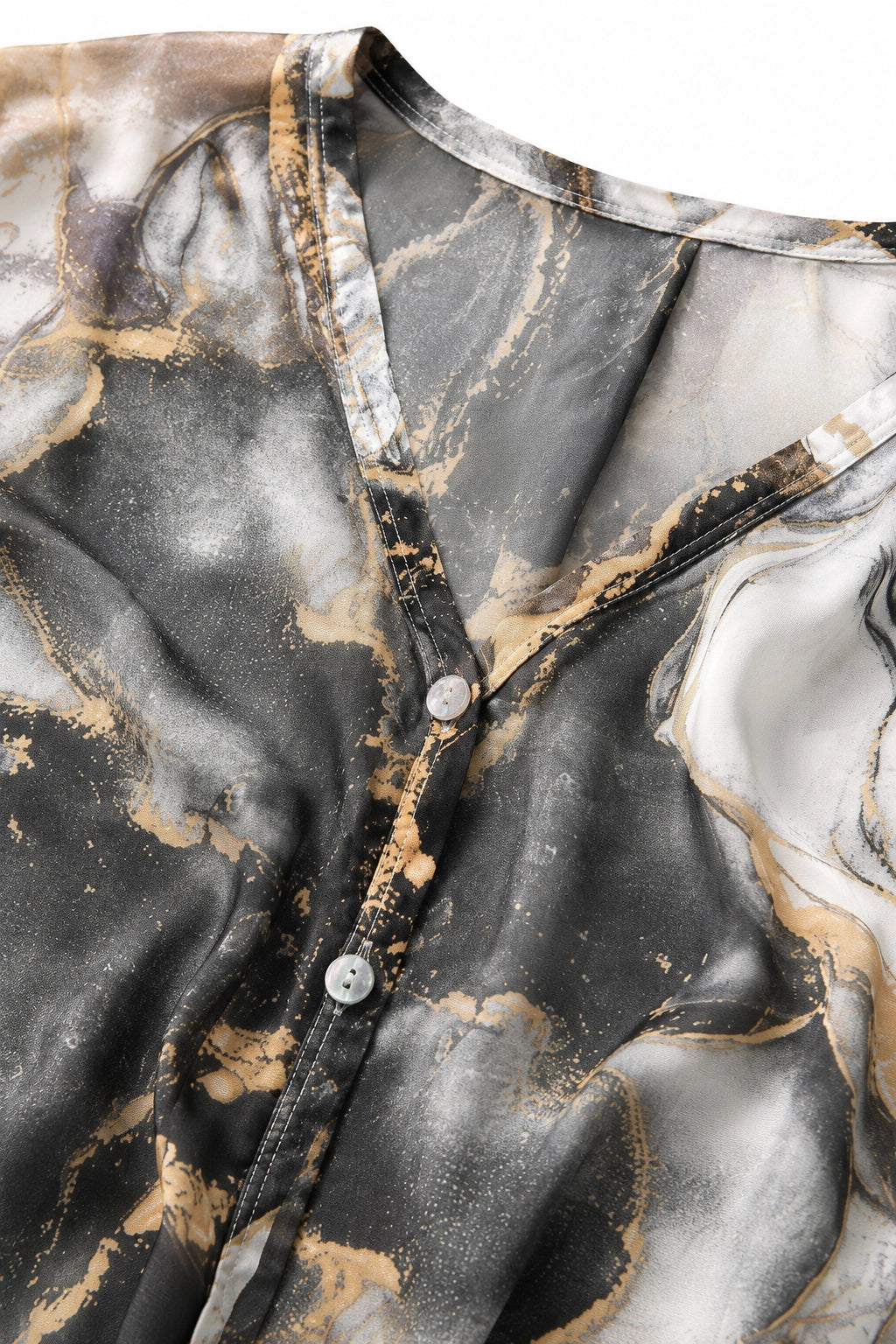 Close-up of a button-front blouse with a marbled abstract print in black, gray, white, and warm beige/gold tones, shown against a plain white background.