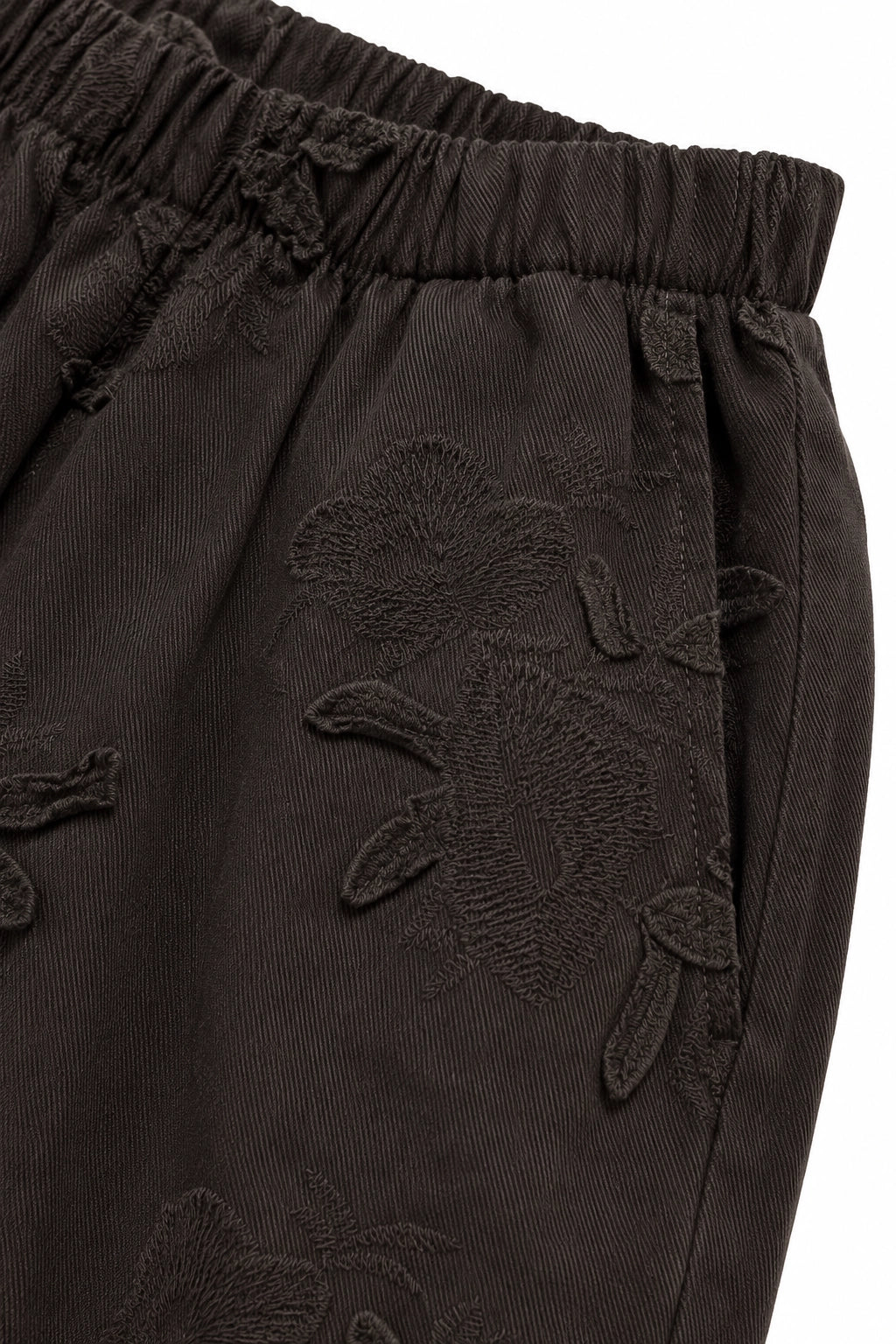 Close-up of dark brown corduroy trousers featuring tonal floral embroidery and an elastic waistband.