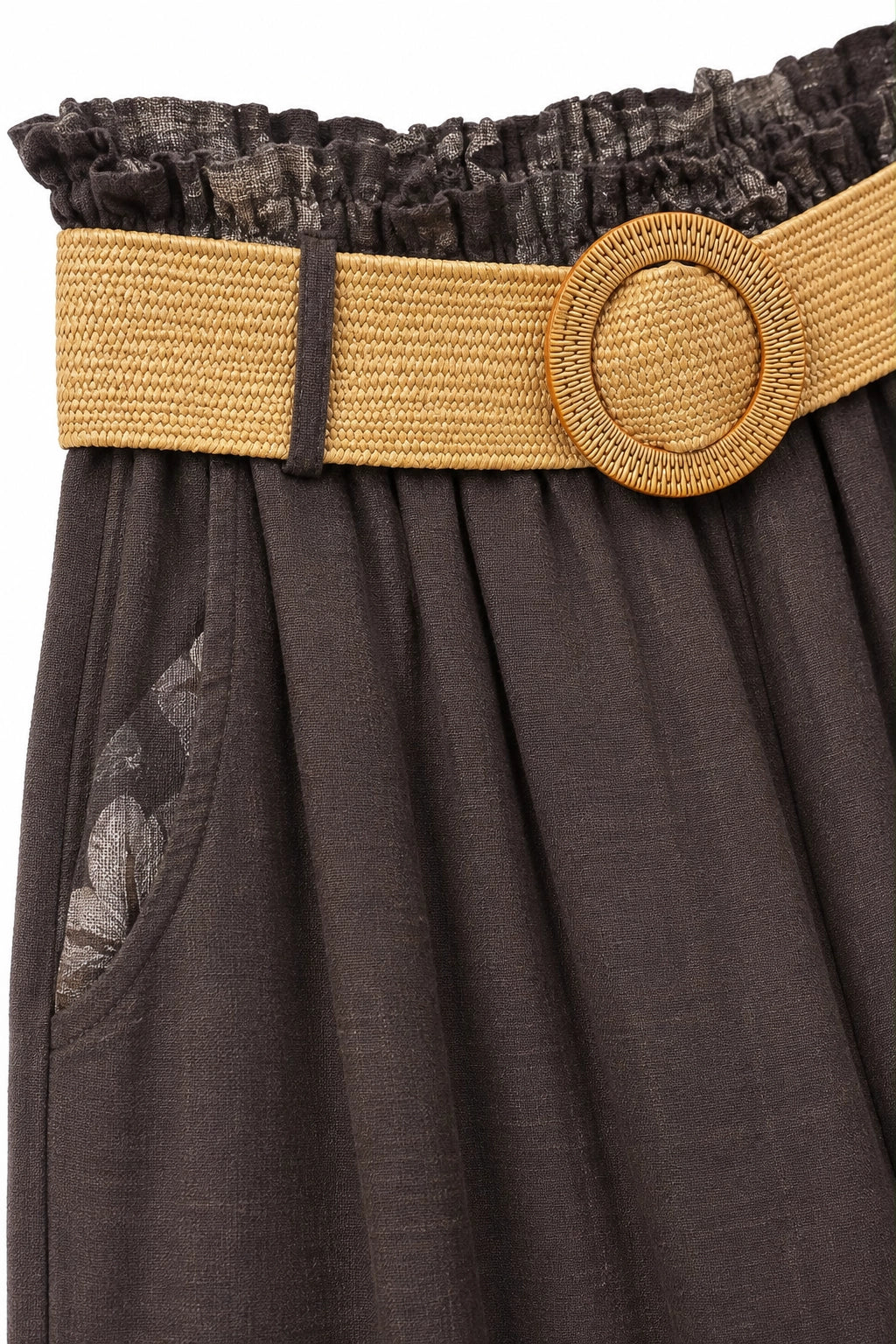 Close-up of a dark brown pleated skirt featuring a wide tan woven belt with a round wooden-style buckle and a ruffled dark waistband.