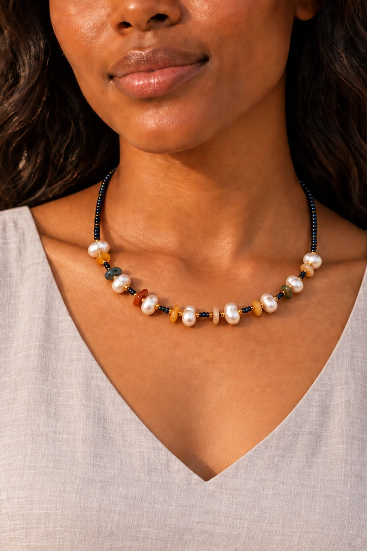 A close-up of a woman wearing a beaded necklace with white pearls and small multicolored beads, paired with a light gray V-neck top.