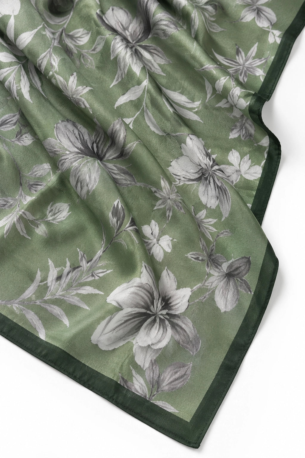 A close-up of a green silk scarf with a gray and white floral print and a solid dark green border, laid out on a white background.