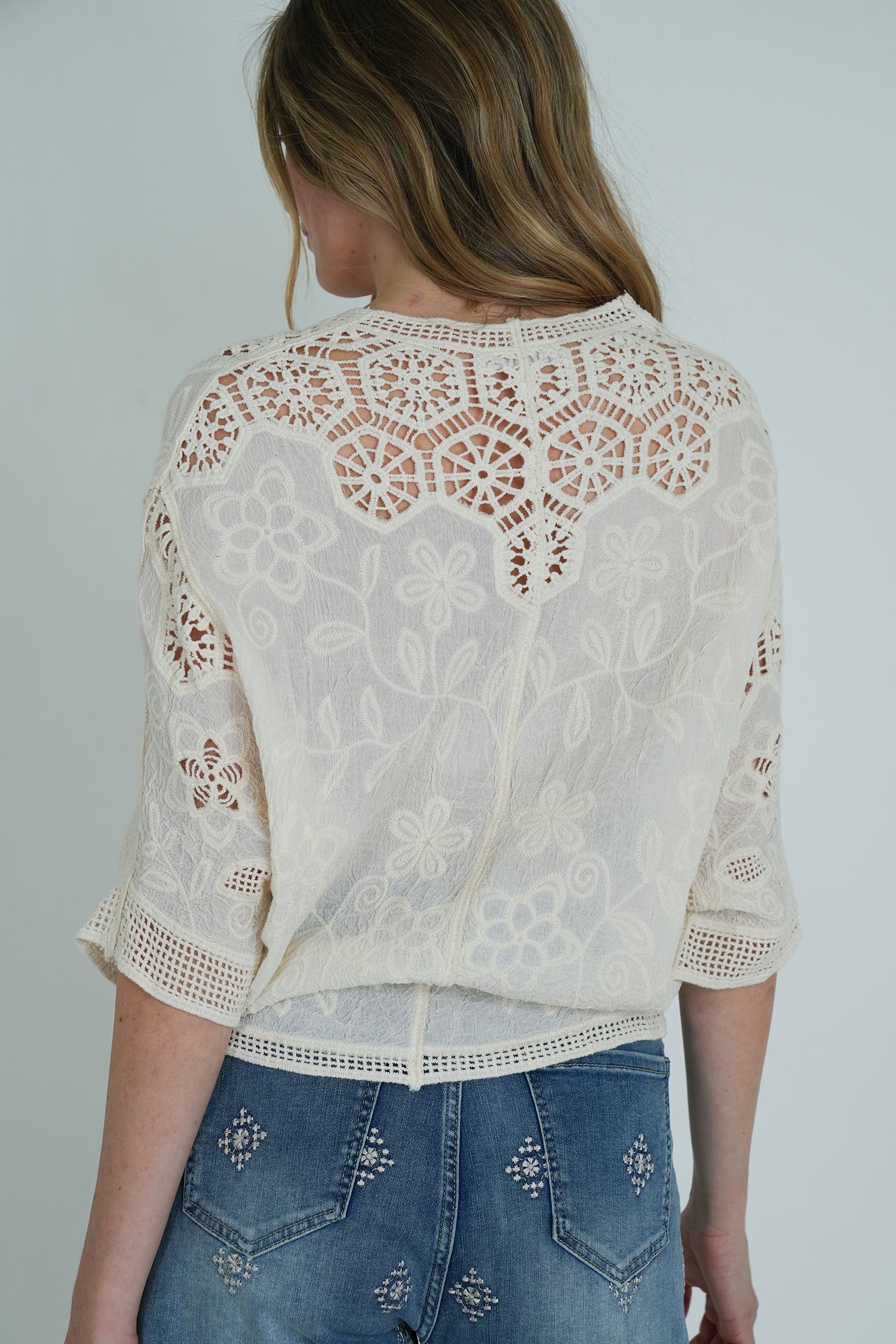 Woman wearing a white lace top and blue jeans against a plain background