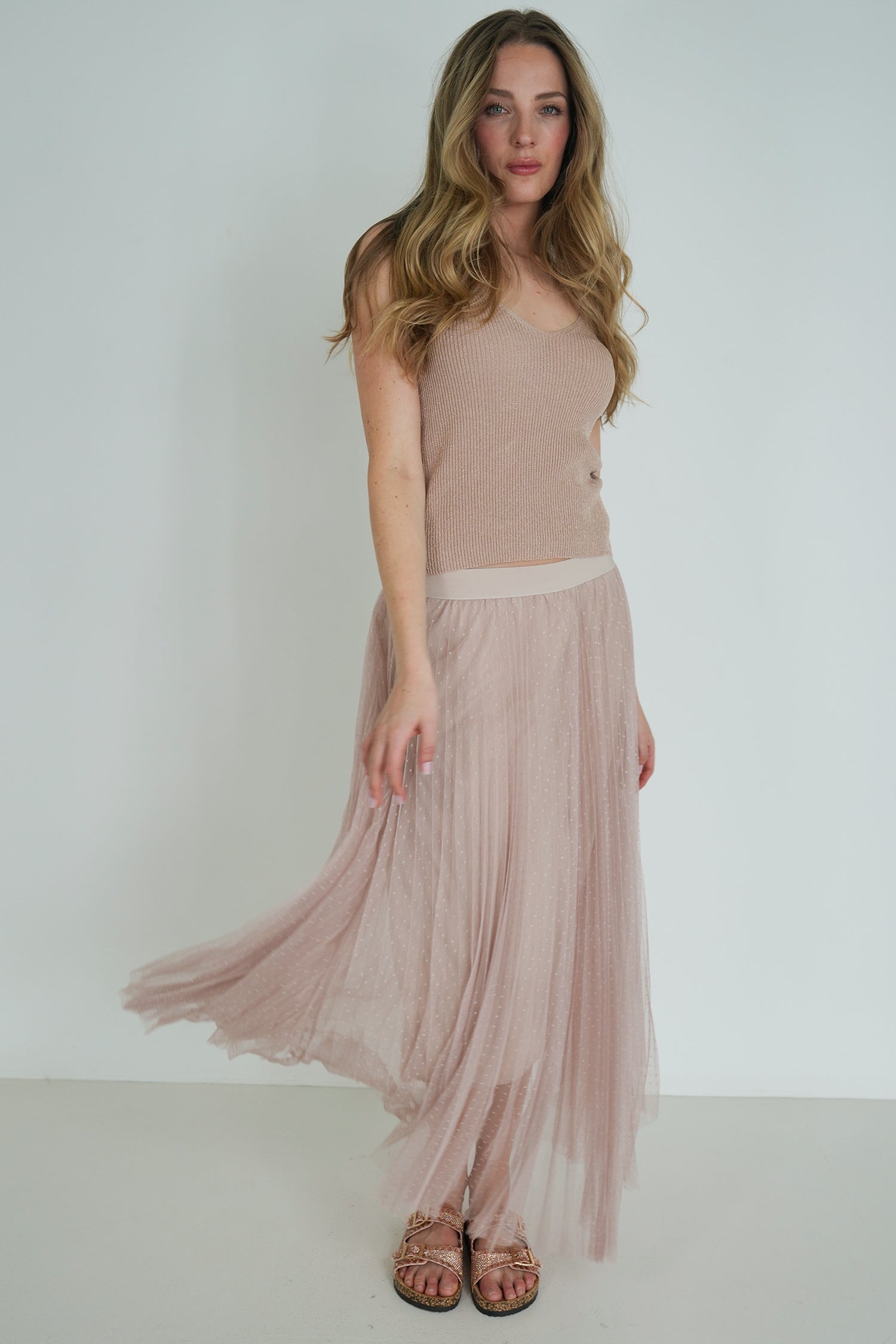 Woman wearing a beige sleeveless top and flowing skirt against a white background