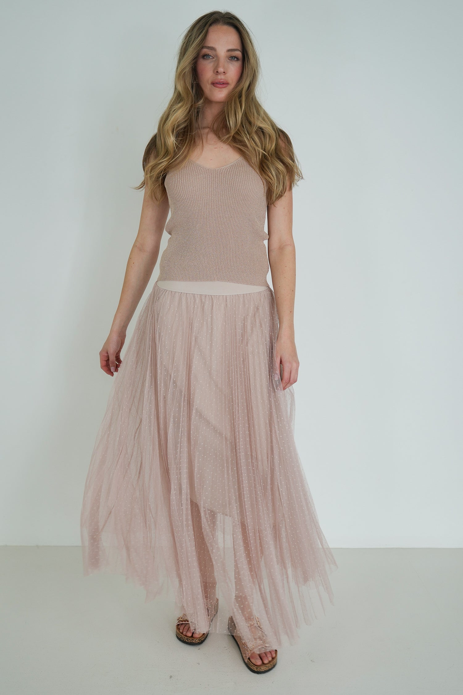 Woman wearing a beige sleeveless top and pleated skirt against a white background