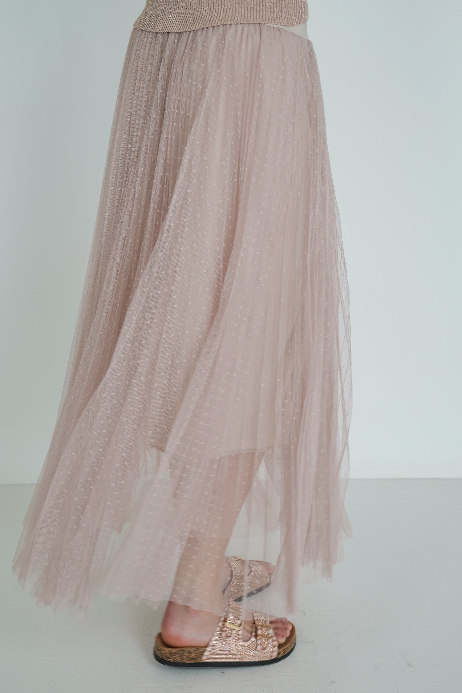 Long beige tulle skirt worn with a top and sandals on a plain background