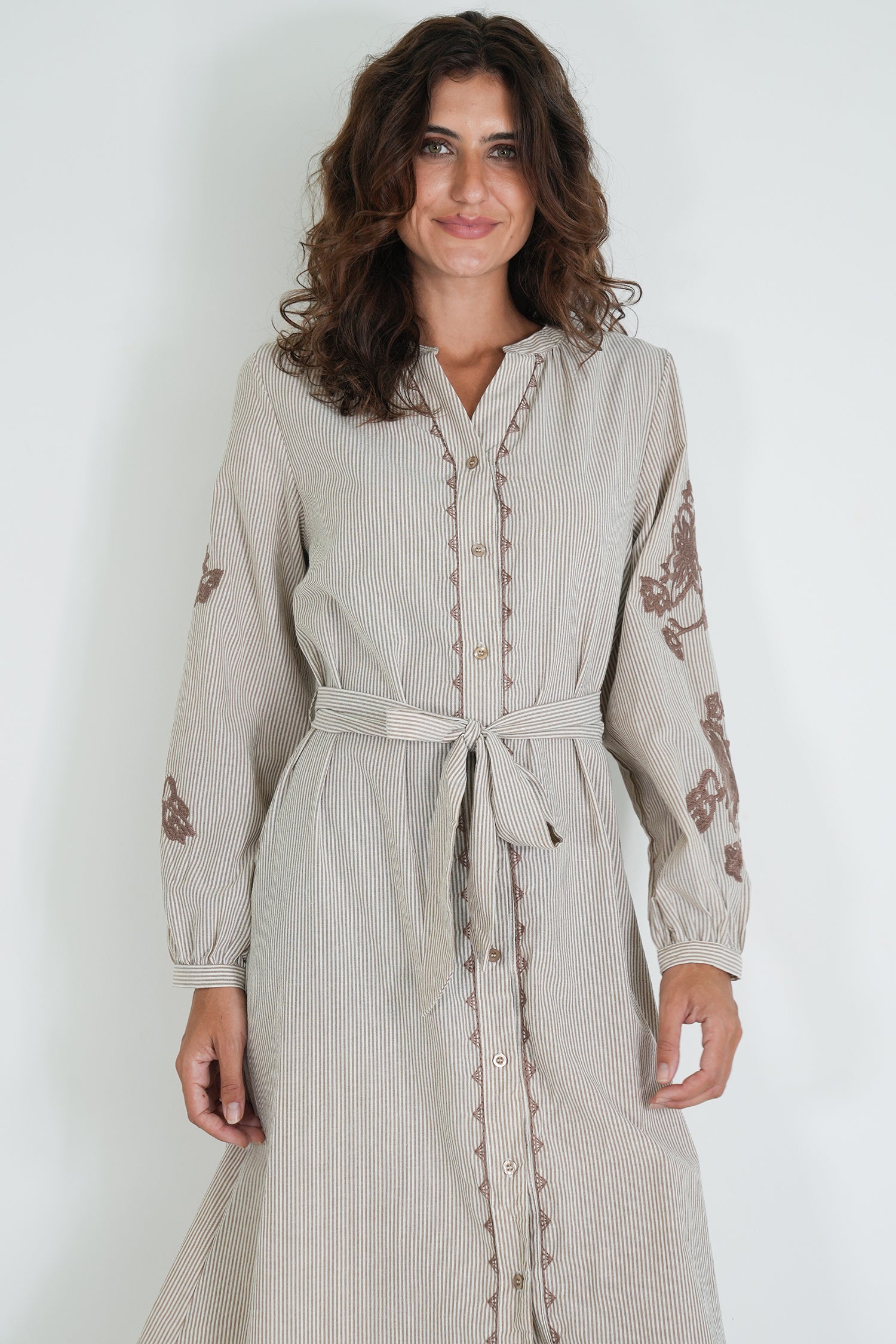 Woman wearing a beige dress with floral embroidery on a white background