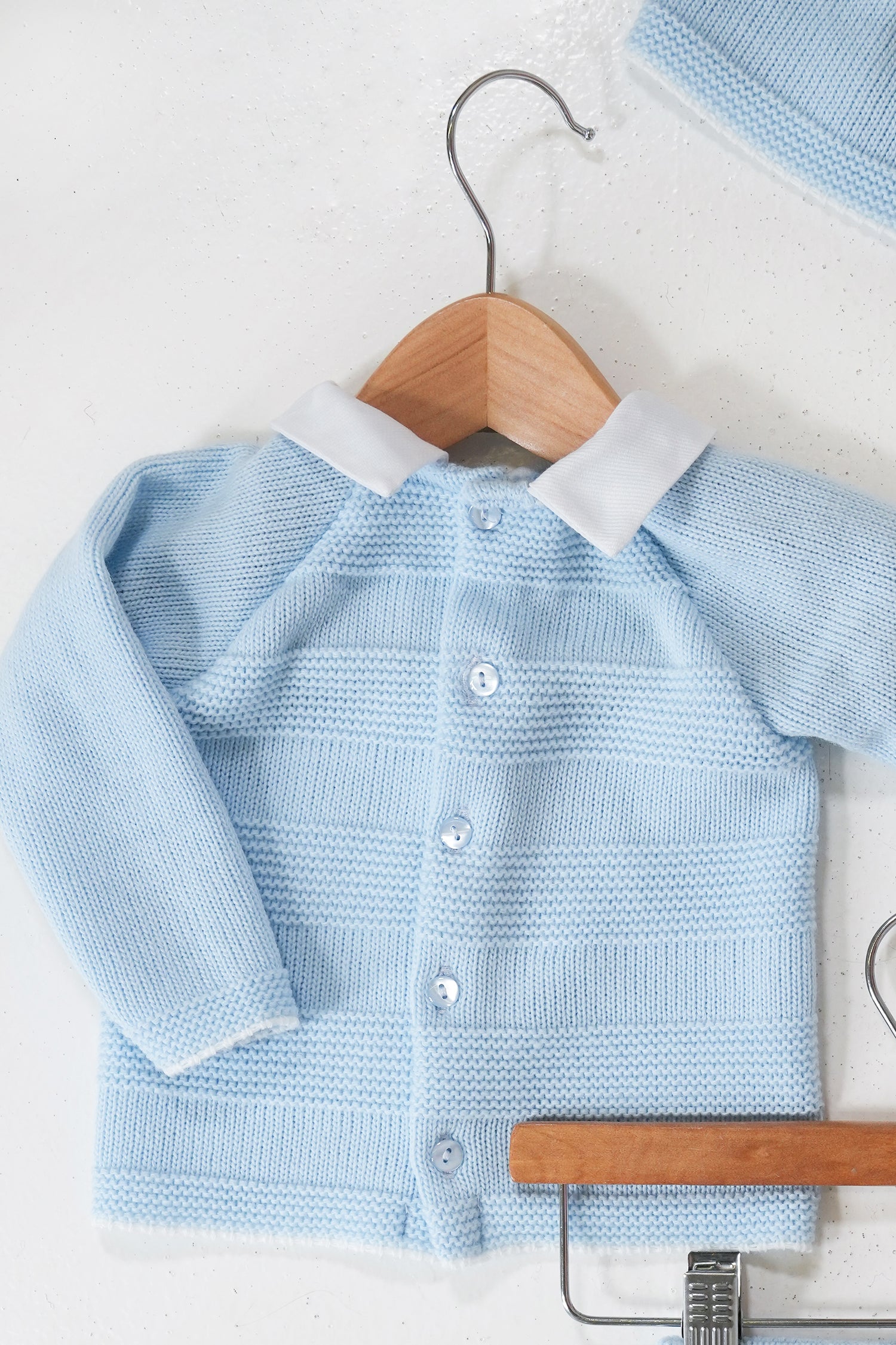 Light blue baby cardigan with white collar on a wooden hanger against a light background