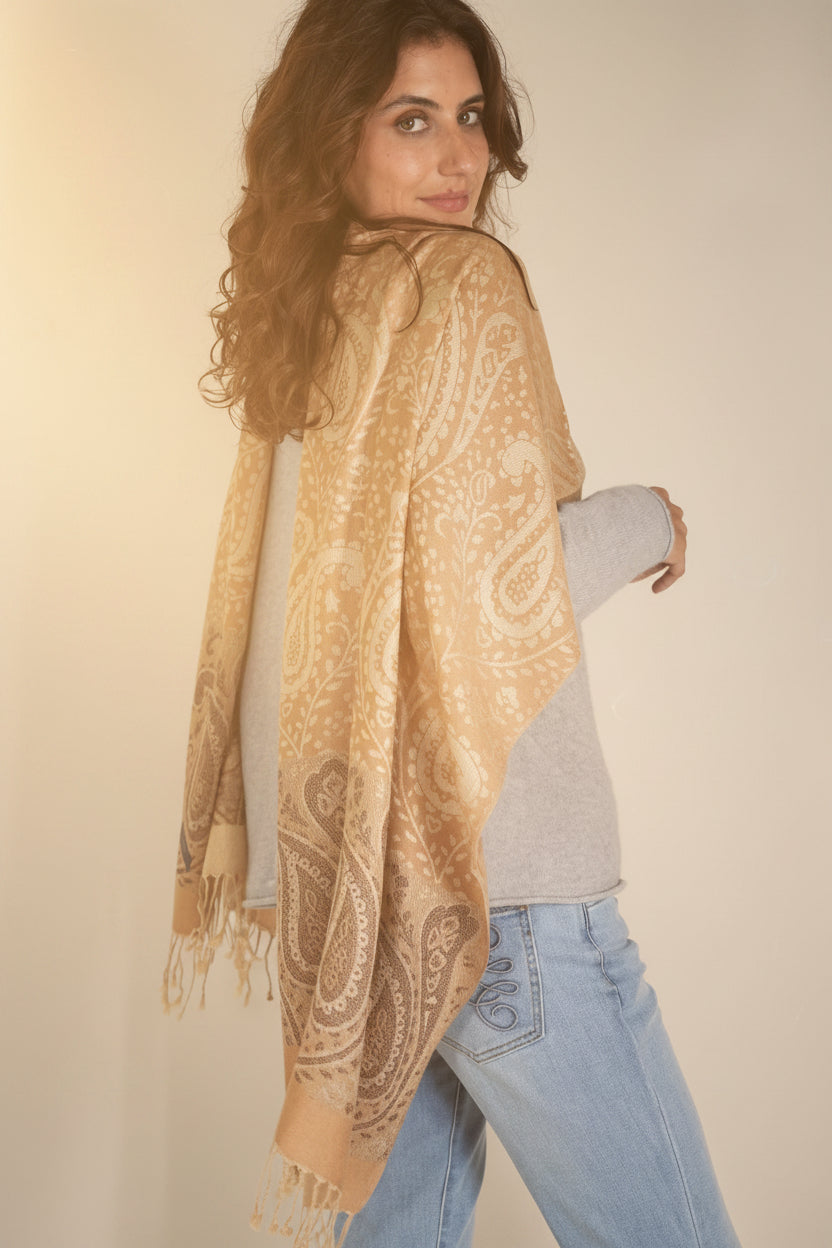Woman wearing a beige paisley scarf, gray sweater, and blue jeans against a white background