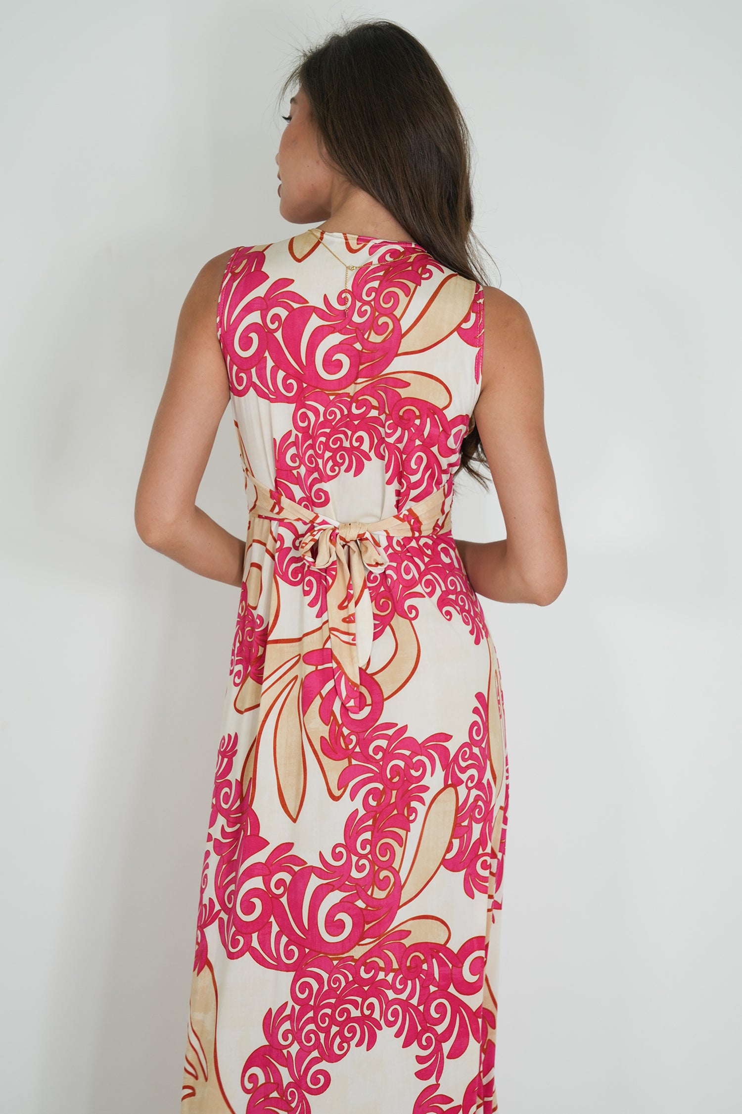 Woman wearing a sleeveless dress with pink and white floral pattern on a plain background