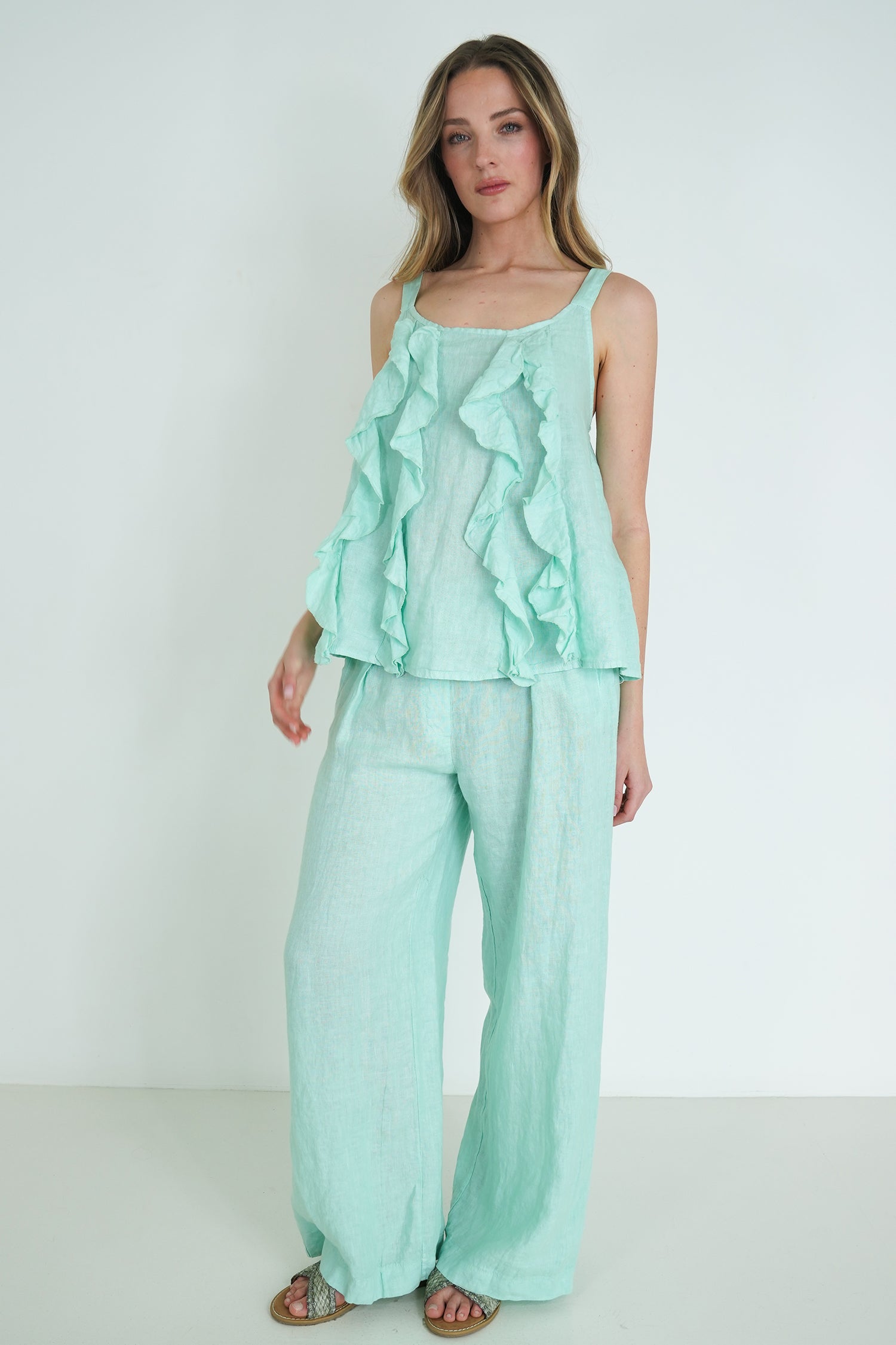 Woman wearing a mint green ruffled top and wide-leg pants on a white background