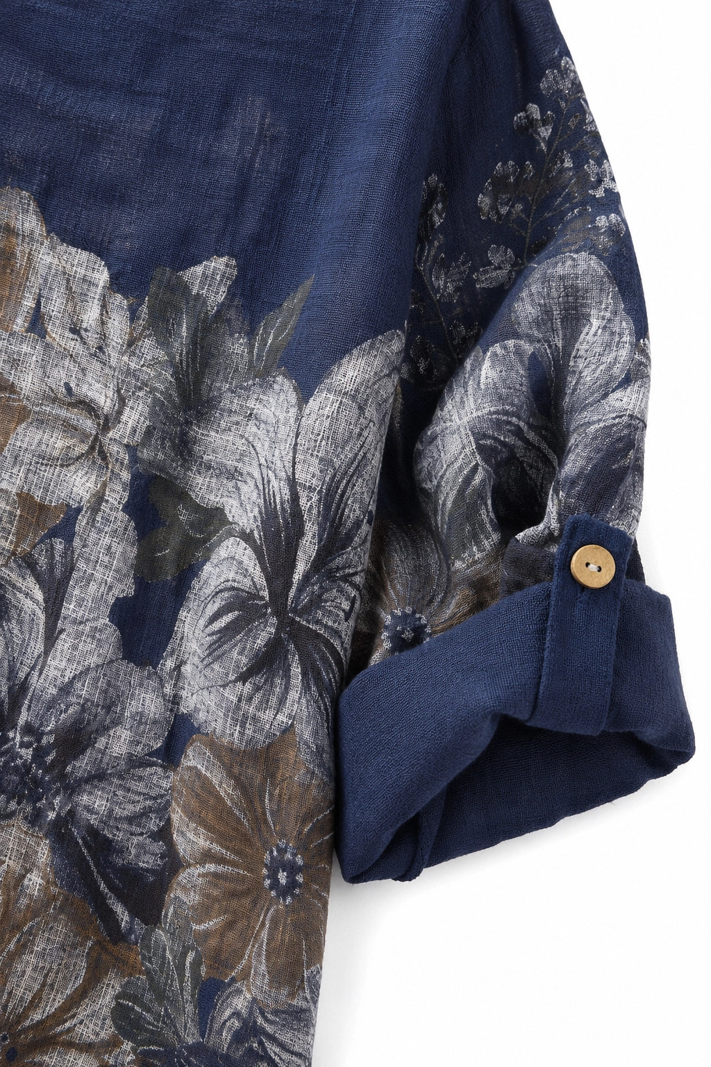 Close-up of a navy blue floral shirt with a large-scale abstract floral print in gray, white, and brown, featuring a rolled cuff with a single gold button.