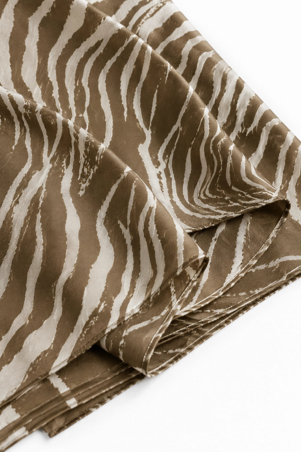A close-up of a draped fabric scarf or shawl with a zebra-like abstract stripe pattern in warm taupe-brown and off-white, folded neatly on a white background.