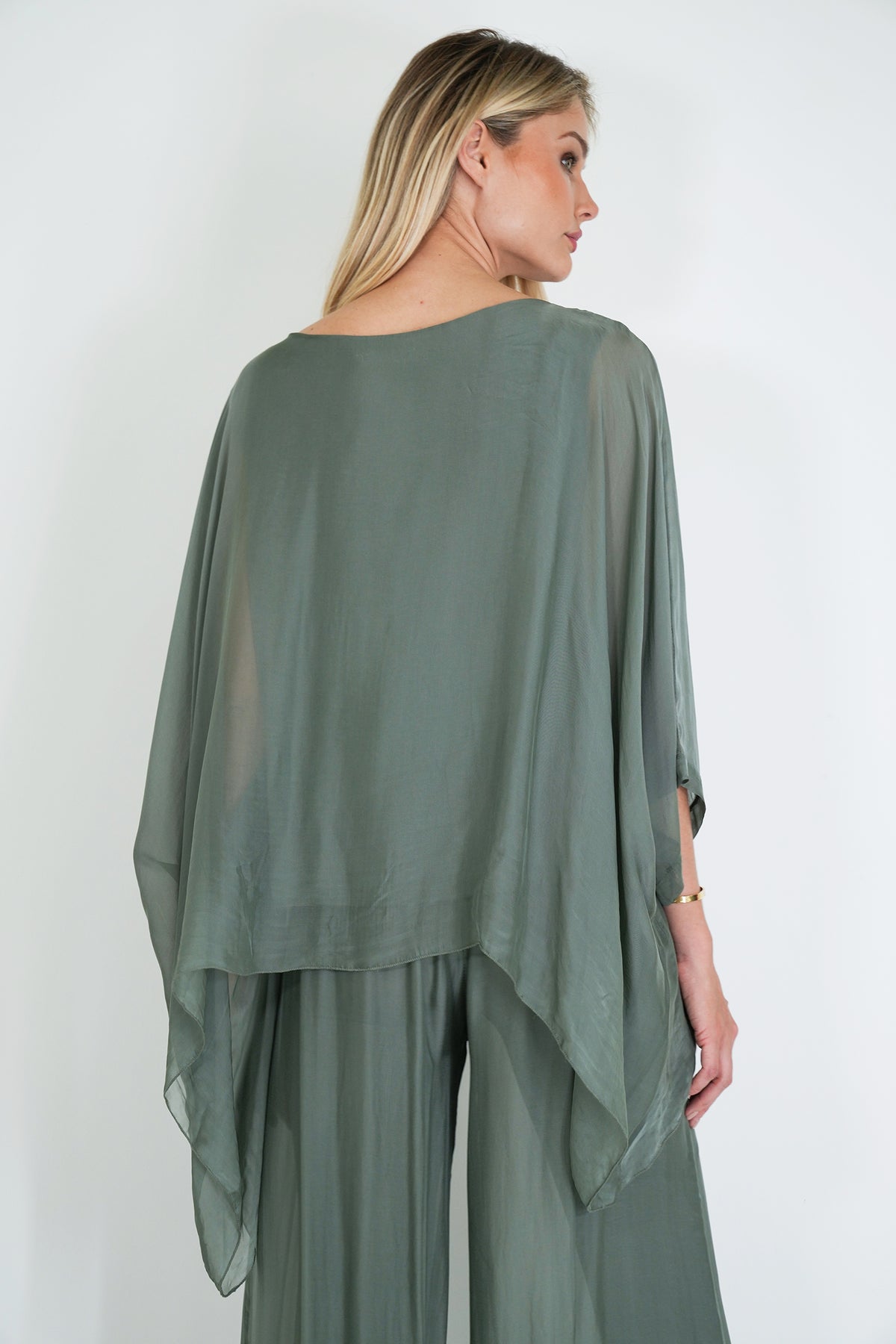 Woman wearing a green outfit with a sheer overlay against a white background
