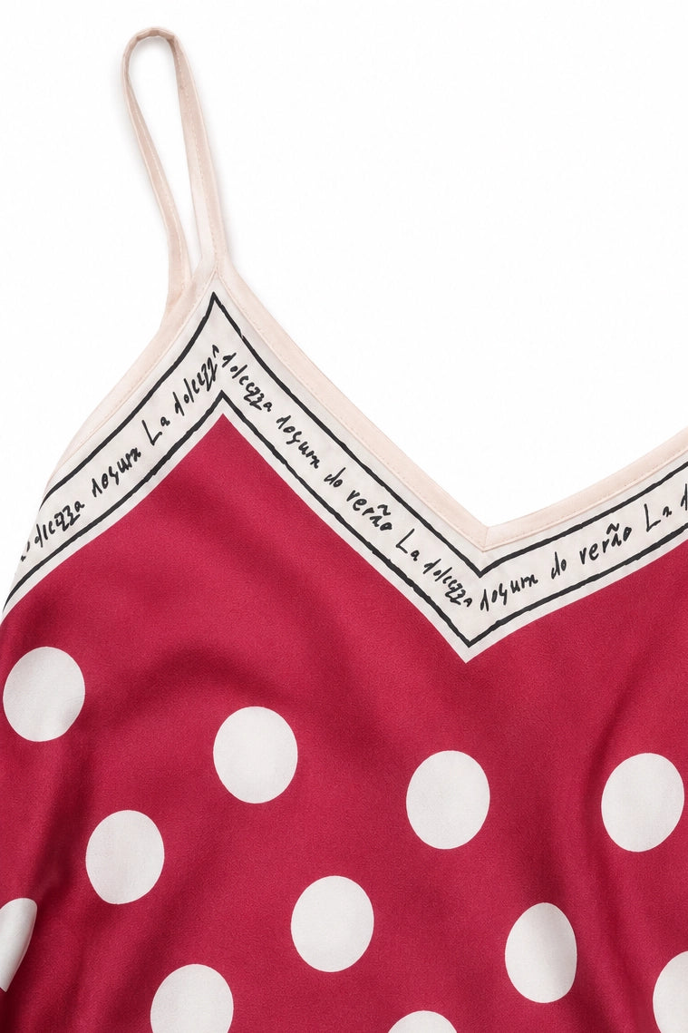 A close-up of a red camisole top with large white polka dots and a cream-colored inner band featuring black script text.
