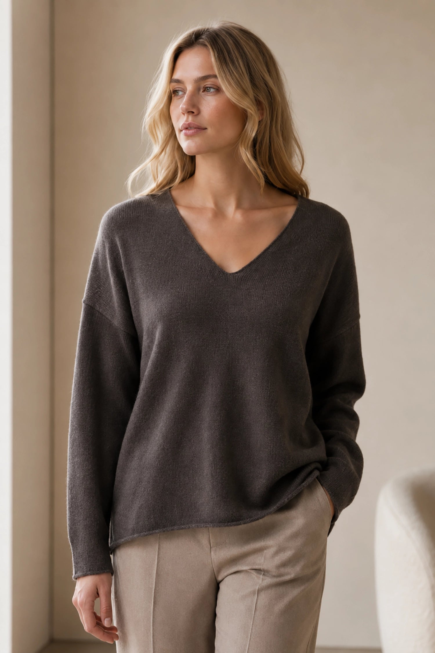 Woman wearing a dark brown sweater and beige pants against a neutral background