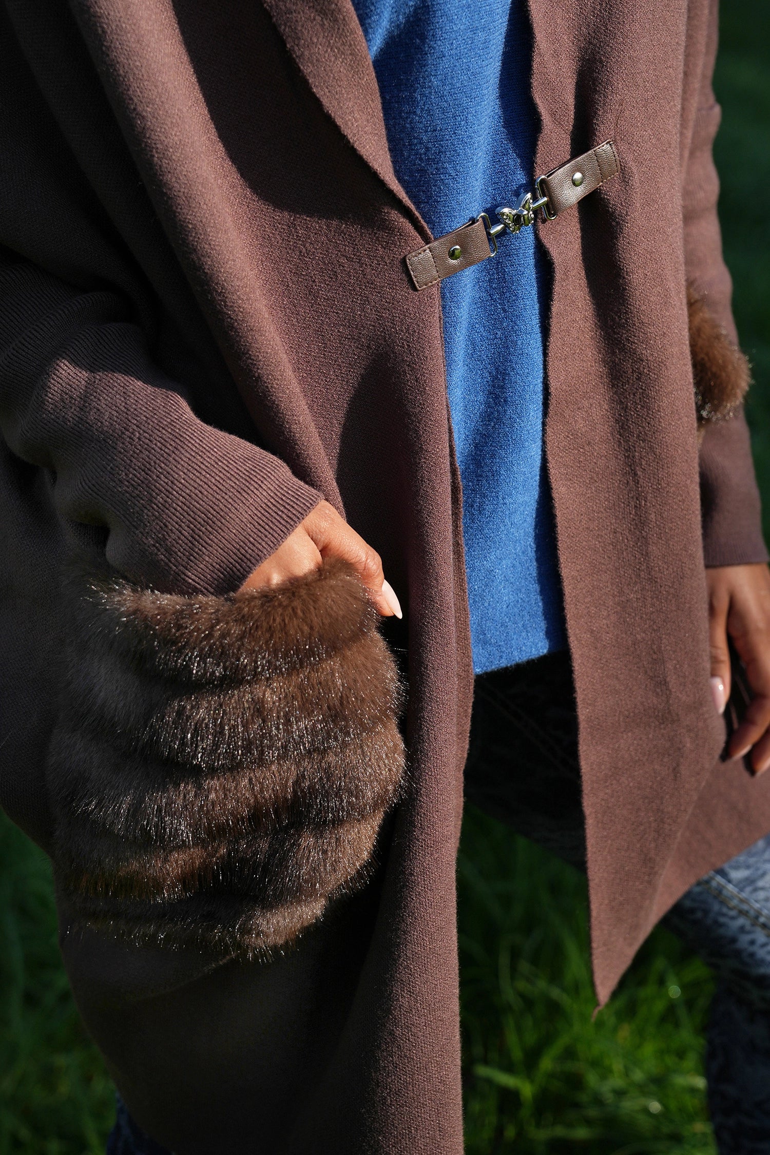Brown coat with fur-trimmed cuffs and a blue shirt underneath, against a blurred green background.