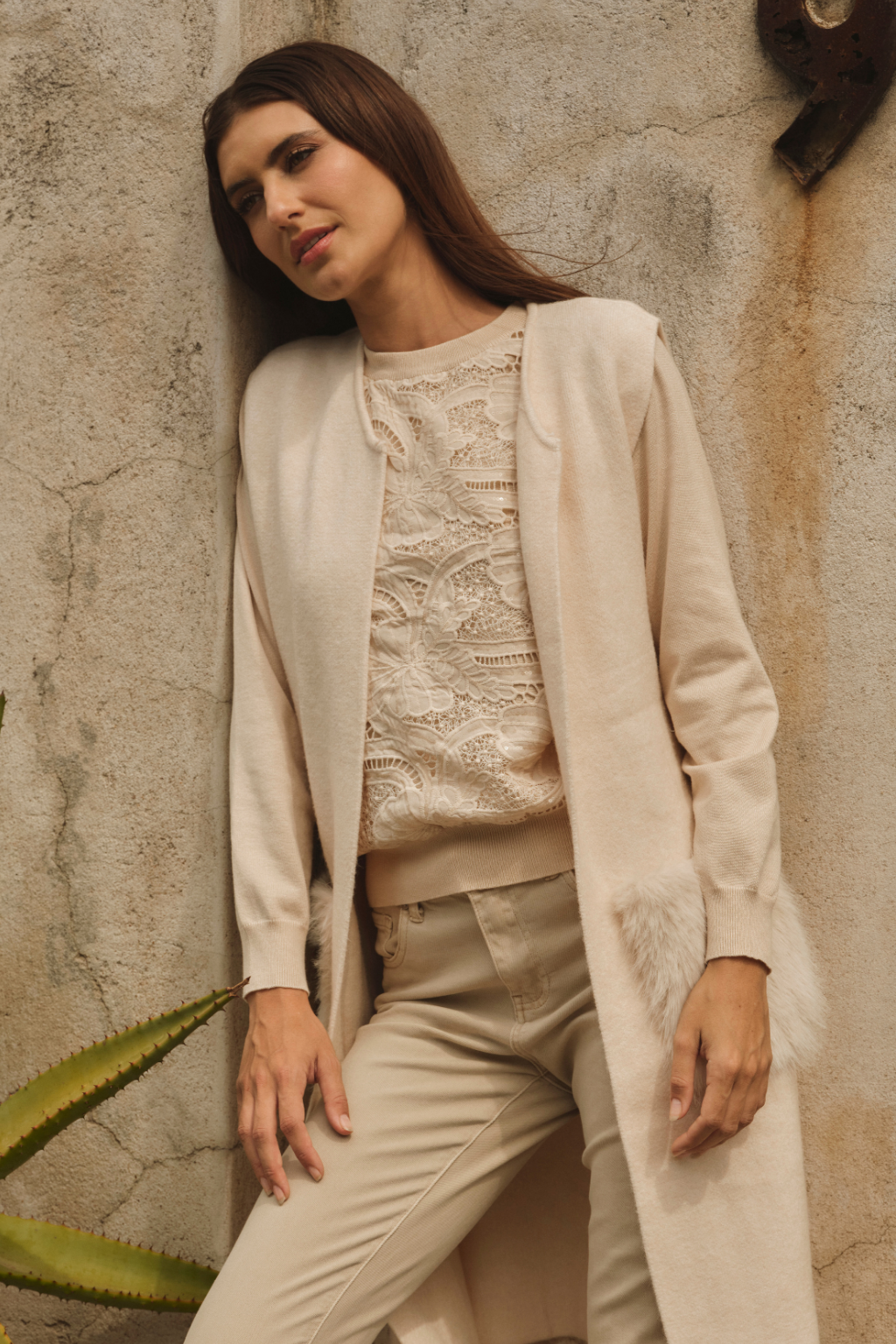 Woman wearing a beige outfit against a textured wall.