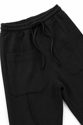 Close-up of black sweatpants showing the elastic drawstring waistband, front patch pockets, and leg construction on a white background.