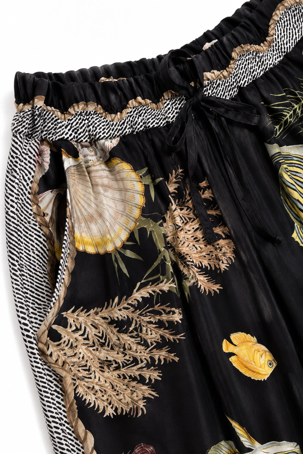 Close-up of a black skirt with an ocean-themed print featuring seashells, coral, and a yellow fish, finished with a patterned drawstring waistband.