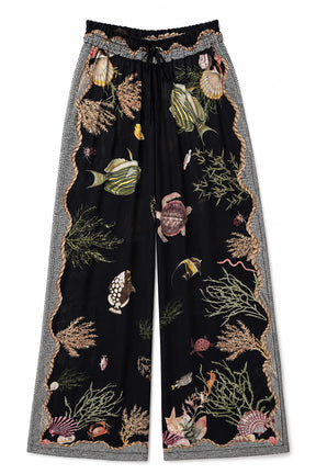 Black wide-leg pants featuring an all-over embroidered underwater theme with fish, sea plants, and shells, framed by a gray and gold patterned border and an elastic drawstring waist.