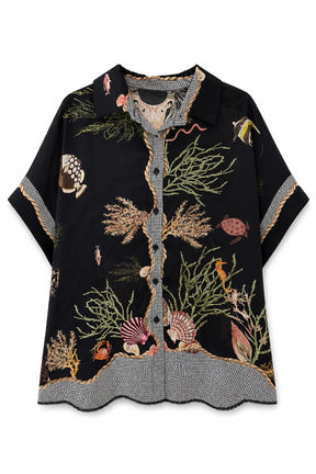 A short-sleeve button-up shirt with a black base and an intricate underwater-themed print featuring seashells, coral, fish, and sea plants. The shirt has a textured gray and white patterned collar, cuffs, and hem, and is displayed flat against a white background.