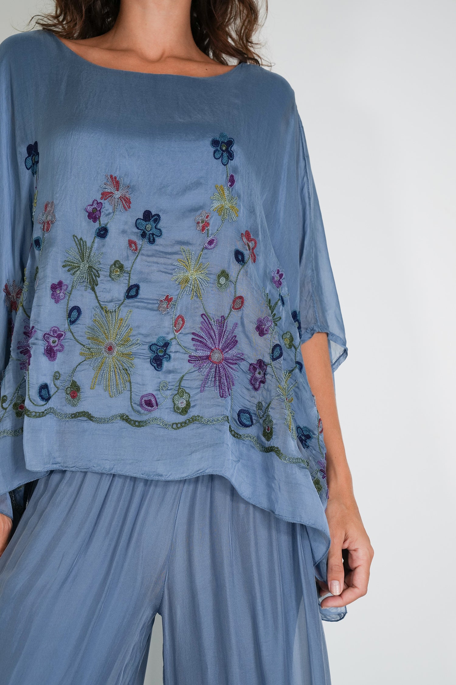 Blue top with floral embroidery worn by a person on a white background