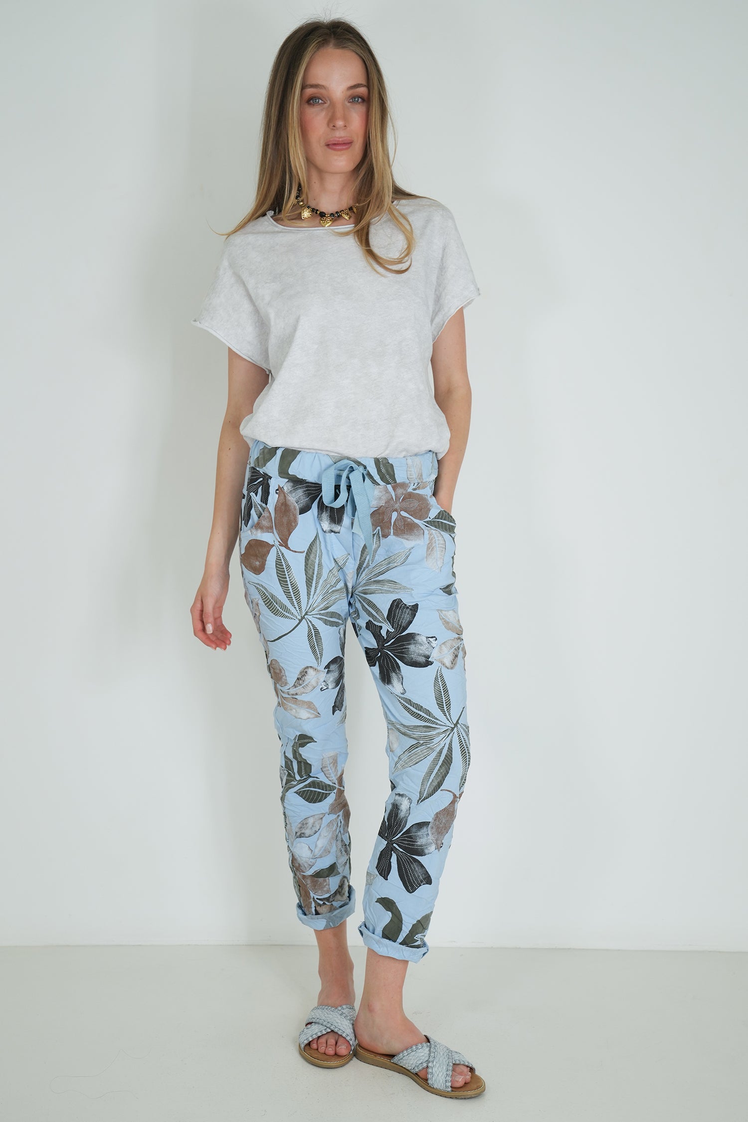 Woman wearing a white t-shirt and floral pants against a plain background