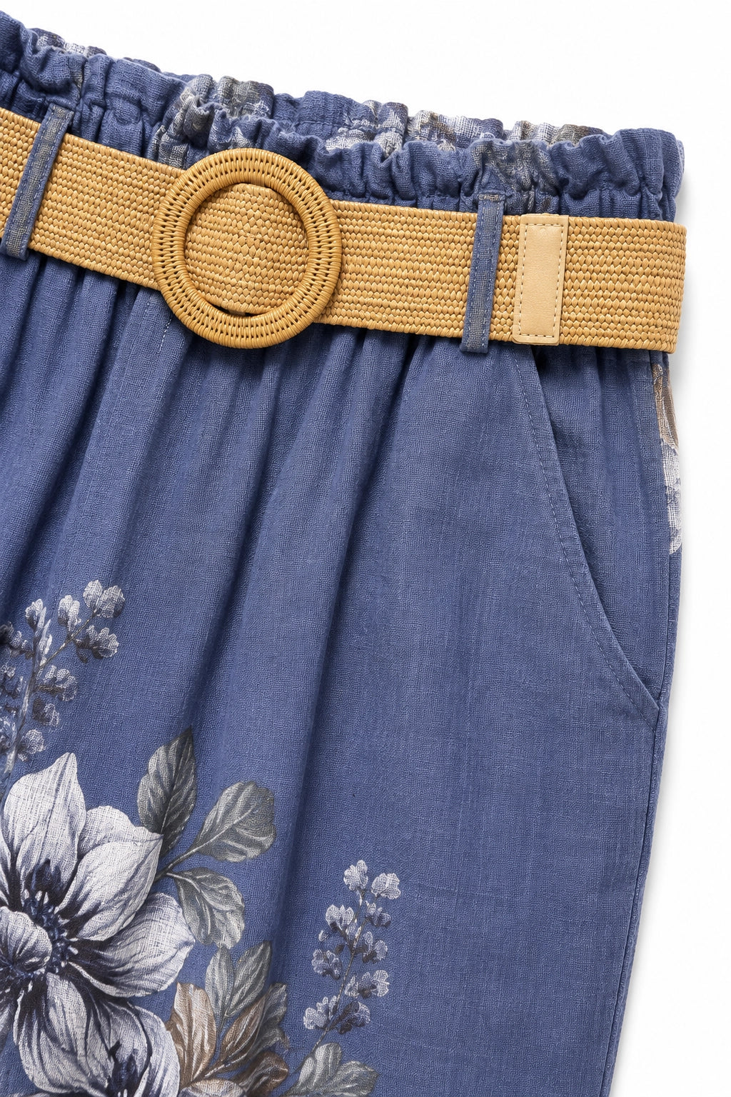 Close-up of a pair of blue floral pants with a wide tan woven belt featuring a round woven buckle, shown against a white background.