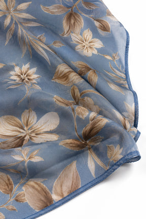 A close-up of a sheer blue scarf with a beige and brown floral print, folded to show its texture and border.