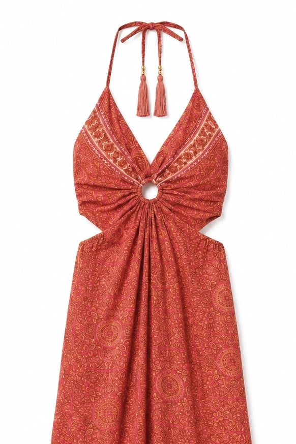 A rust-orange halter dress with a tie-front knot and tassel details, featuring a subtle circular pattern and embroidered trim on the neckline, shown against a plain white background.