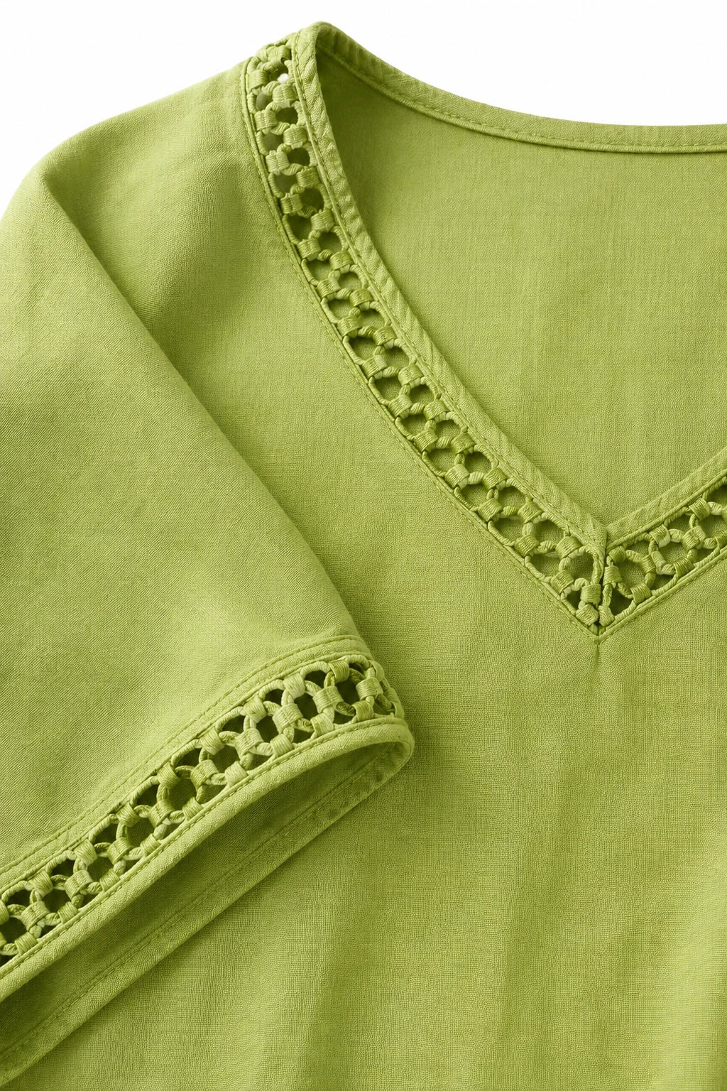 A close-up of a light olive green short-sleeve top with a V-neckline and matching eyelet lace trim on the collar and sleeve cuff.