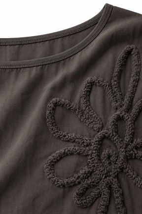 Close-up of a dark brown or charcoal gray top with a large textured floral applique on the chest.