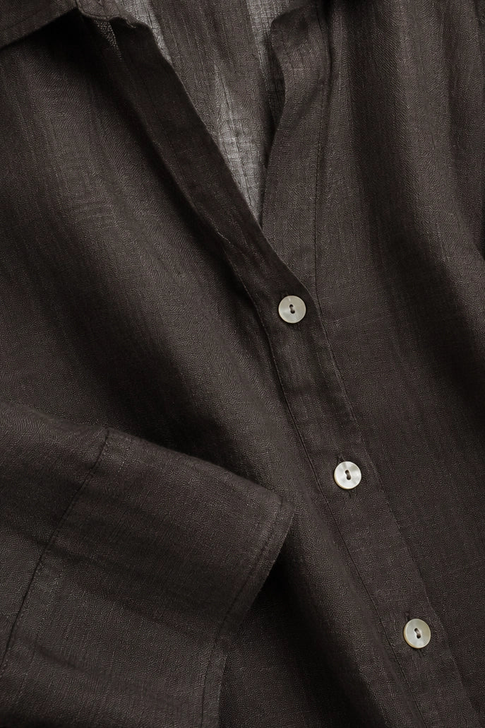 Close-up of a dark brown linen button-down shirt showing the textured fabric and white buttons.