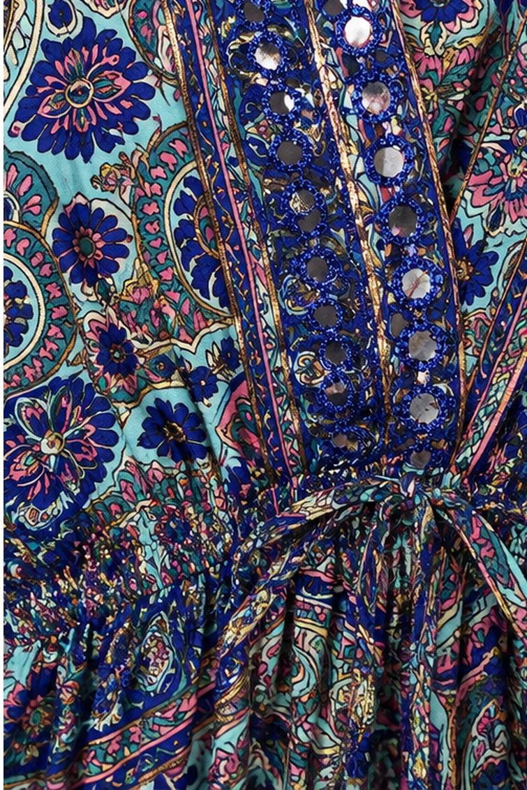 Close-up of a colorful paisley printed fabric with blue, pink, and turquoise tones, featuring a gathered waist tie and decorative mirror-like embellishments.