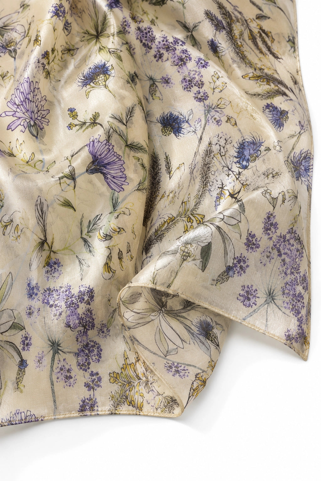 A close-up of a lightweight scarf or fabric with a delicate botanical print on a warm beige background, featuring purple flowers and green leaves, draped elegantly on a white surface.