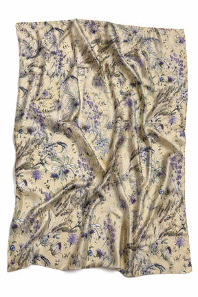A lightweight, semi-sheer scarf with a beige base and an all-over floral pattern in shades of purple, blue, and green, draped in soft folds against a white background.