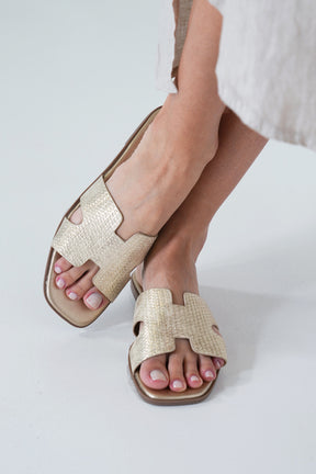 Gold sandals worn by a person on a white background