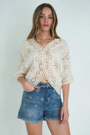 Woman wearing a white lace top and blue denim shorts on a plain background