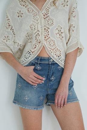 Person wearing a lace top and denim shorts on a white background