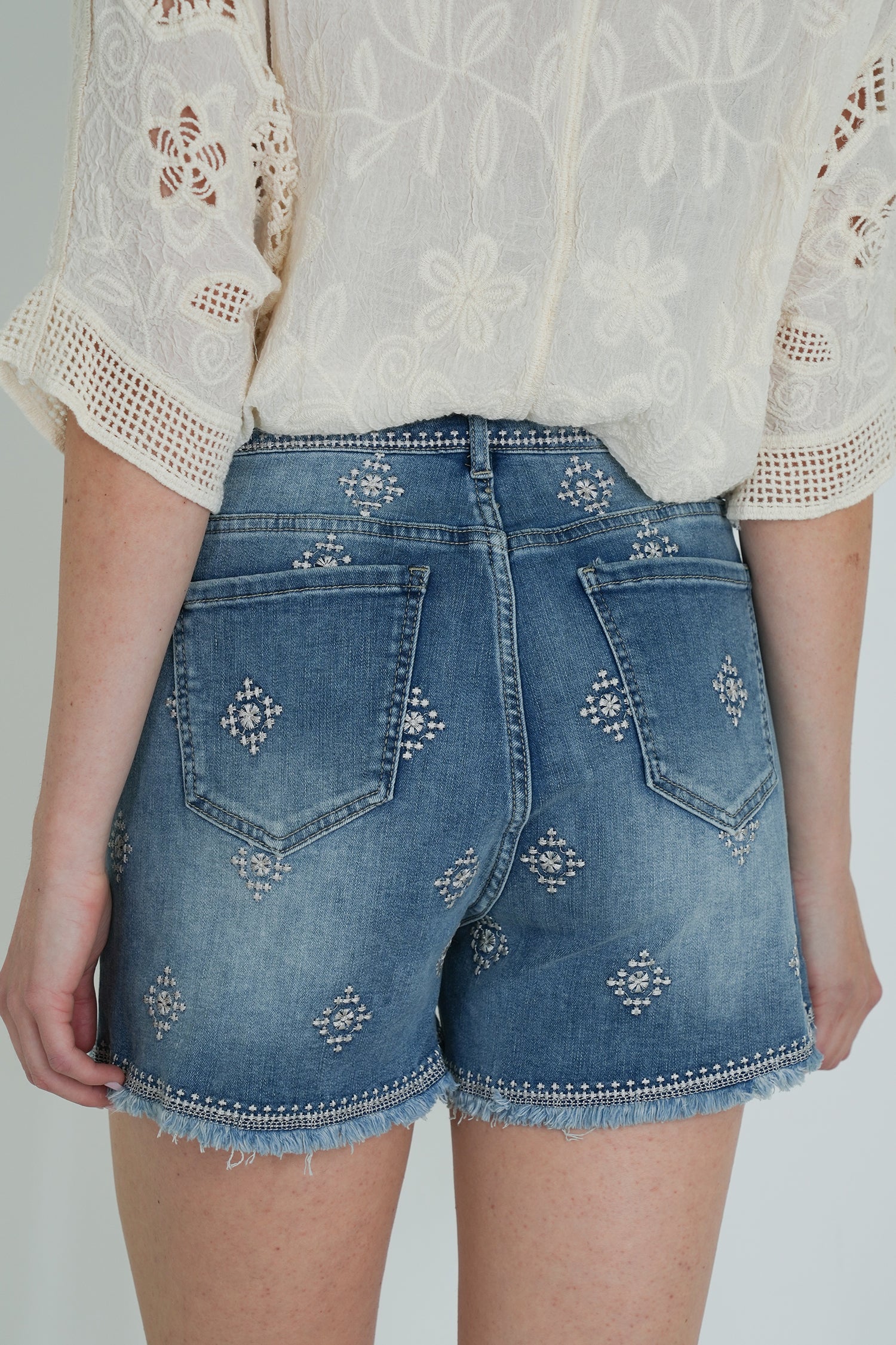 Denim shorts with decorative elements worn by a person on a plain background