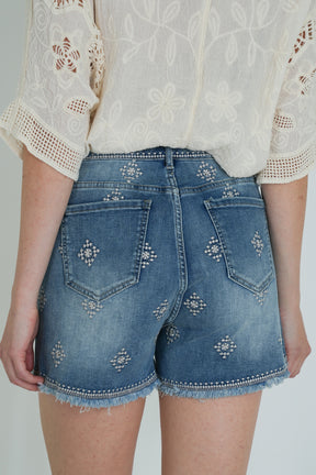 Denim shorts with decorative elements worn by a person on a plain background