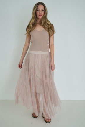 Woman wearing a beige sleeveless top and pleated skirt against a white background