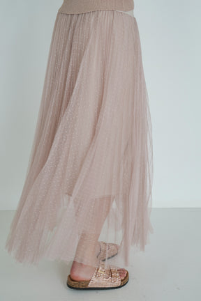 Long beige tulle skirt worn with a top and sandals on a plain background