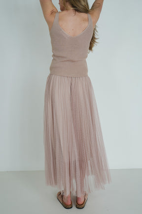 Woman wearing a beige sleeveless top and pleated skirt against a white background