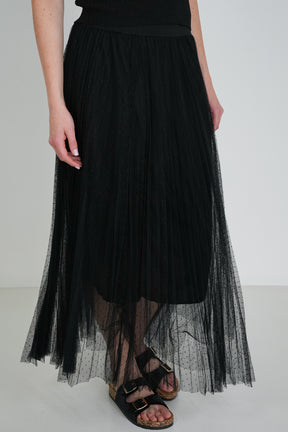 Close-up of black pleated tulle midi skirt with sheer overlay, showing waist detail and black sandals with gold buckles.