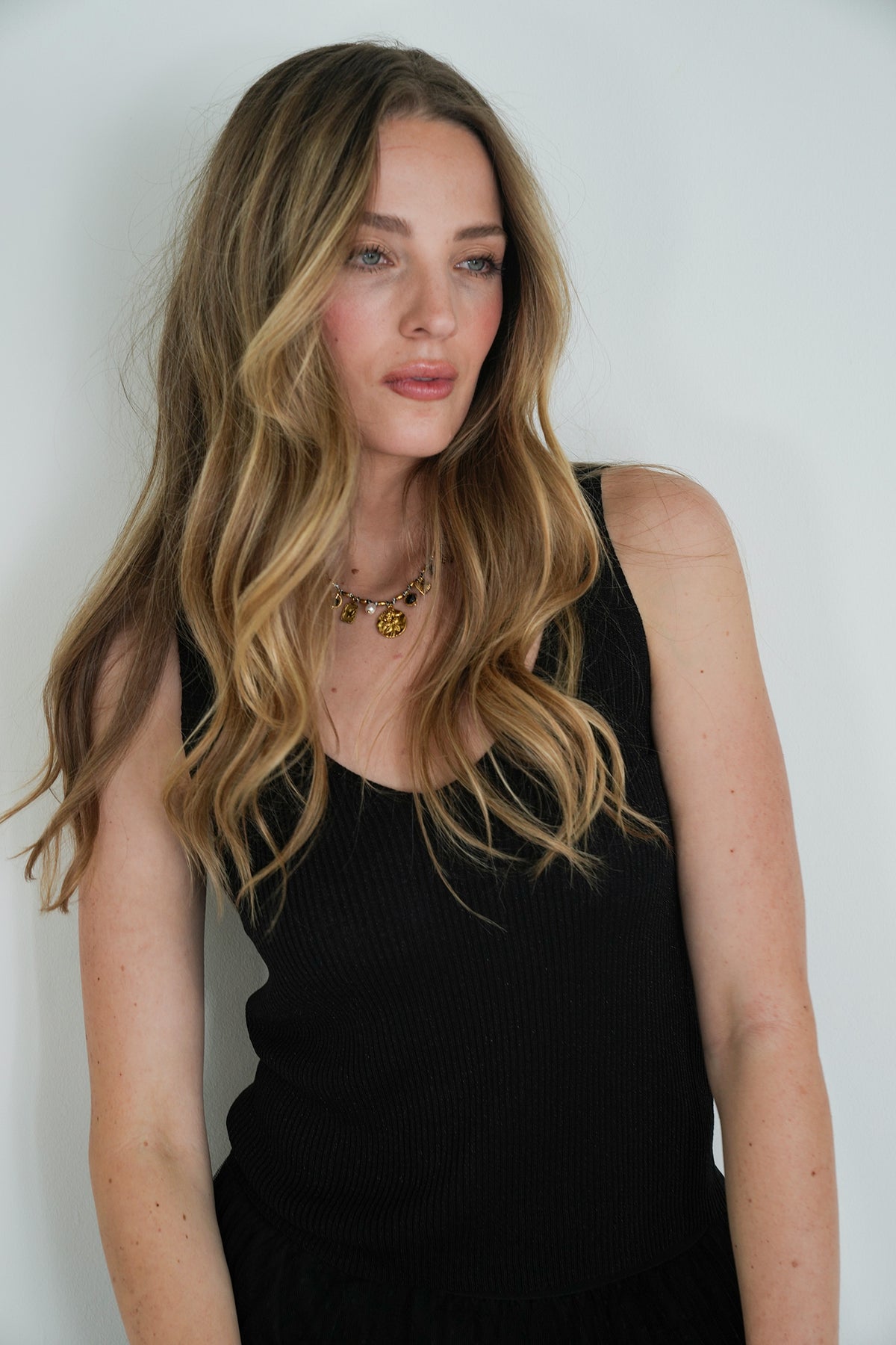 Woman with long blonde hair wearing a black sleeveless top against a white background
