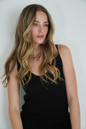 Woman with long blonde hair wearing a black sleeveless top against a white background