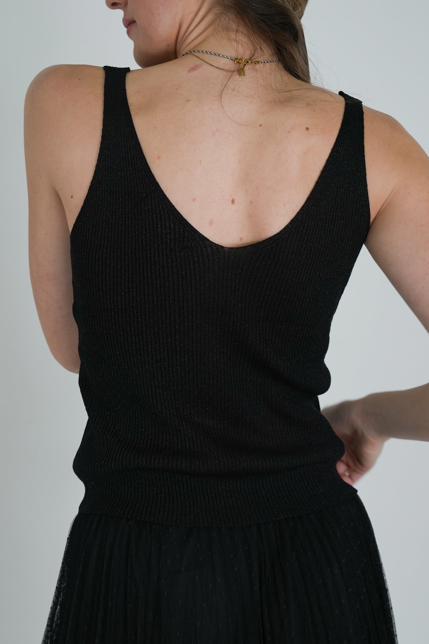 Back view of model wearing a sleeveless black ribbed V-neck top tucked into a black tulle skirt, showing textured fabric detail.