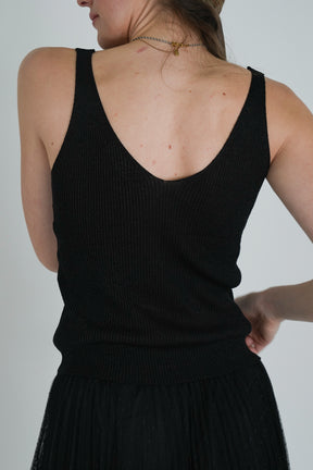 Back view of model wearing a sleeveless black ribbed V-neck top tucked into a black tulle skirt, showing textured fabric detail.